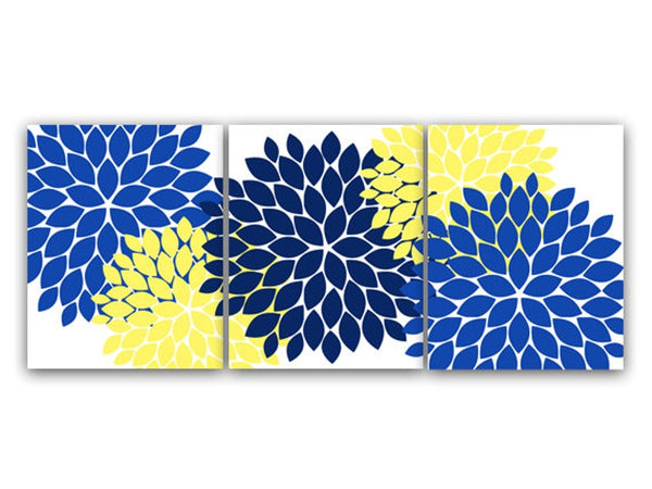 A set of three canvas paintings featuring a navy blue, blue, and yellow dahlia flower petal burst pattern on a white background, intended for use as bathroom, bedroom, nursery, or other room's wall decor.