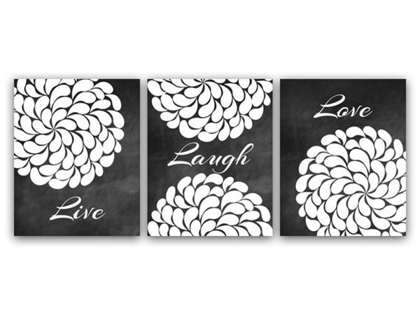 A three panel set of wall art prints with a black chalkboard background & white flower petal swirl, and white script with the words 'Live', 'Laugh', and 'Love' - one word on each panel. The left panel has a white flower petal swirl with the word 'Live' at the bottom. The center panel has 1/2 of a white flower petal swirl at the top and 1/2 at the bottom with 'Laugh' in the middle. The right panel has a white flower petal swirl with the word 'Love' at the top.