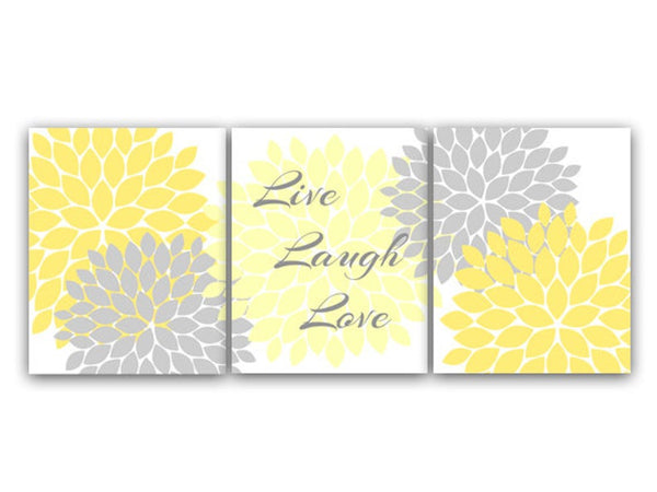 A set of three wall art prints featuring a floral burst design in yellow and gray colors with the words 'Live', 'Laugh', and 'Love' displayed across three lines on the center panel in gray script over a light yellow flower burst. The left and right panels feature two flower bursts each - one gray and one yellow. The background on each panel is white.