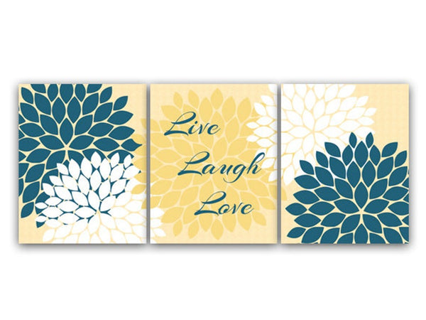 A set of three wall art prints featuring a floral burst design in yellow and teal colors with the words 'Live', 'Laugh', and 'Love' displayed across three lines on the center panel in steel blue script over a yellow flower burst. The left and right panels feature two flower bursts each - one white and one steel blue. The background on each panel is light yellow.